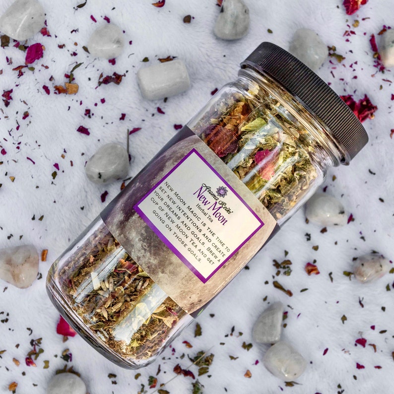 May include: A glass jar filled with dried herbs and flowers, labeled "Aroma Reiki New Moon Herbal Tea". The label includes the text "New Moon Magic is the time to set new intentions and create your dreams and goals. Brew a cup of New Moon Tea and get going on those goals."