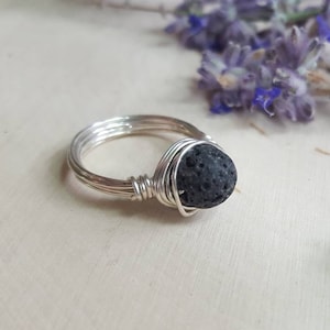May include: A silver wire wrapped ring with a black lava rock bead.
