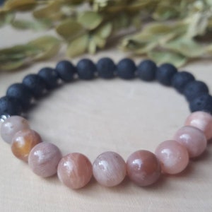 May include: A bracelet made with black lava rock beads and sunstone beads. The bracelet has a two-tone design with the lava rock beads on one half and the sunstone beads on the other half.