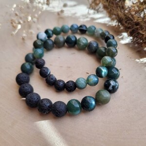 May include: Two bracelets, one made of black lava rock beads and the other made of green agate beads.