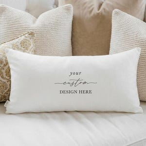 May include: A rectangular white throw pillow cover featuring the centered black text "your custom DESIGN HERE" in a combination of serif and script fonts. The fabric has a smooth, matte finish and a clean, minimalist aesthetic for home decor.