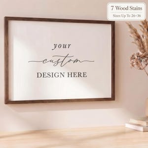 May include: A rectangular wooden picture frame with a white insert featuring the black text your custom DESIGN HERE. A small white label in the top right corner displays the text 7 Wood Stains and Sizes Up to 26x36 inches.