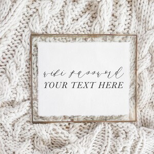 May include: A framed white paper with the words "wifi password" and "YOUR TEXT HERE" in elegant black script. The frame is a thin, gold-colored metal. The background is a textured, off-white knitted fabric.