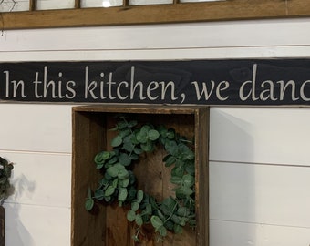 S 230 Handmade, Wood, Long Sign with saying. "In this kitchen, we dance "  44 x 5 1/2 x 3/4. Antiqued, warm. Saying with a comma.