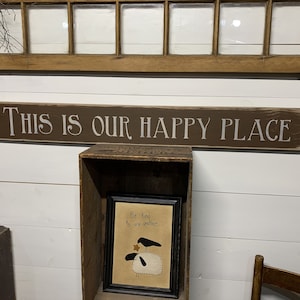 May include: A brown wooden sign with white lettering that reads "This is our happy place".
