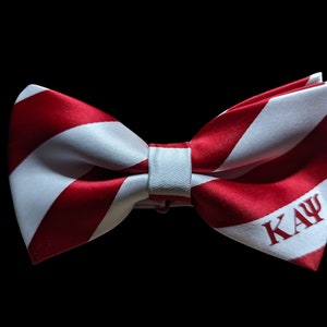 May include: Red and white striped bow tie with the letters "KAYΨ" in red on the white stripe.