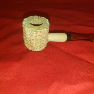 Puede incluir: Una pipa de mazorca de maíz con una boquilla blanca y una boquilla marrón. La pipa está hecha de materiales naturales y tiene un aspecto rústico.