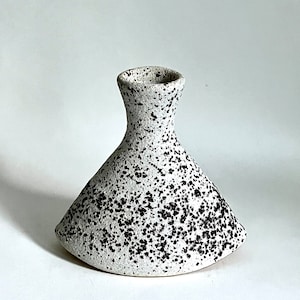 May include: A white ceramic vase with black speckles. The vase has a wide base and a narrow neck.