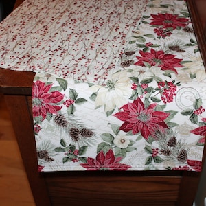 May include: Two white table runners with a Christmas theme. One runner features a red poinsettia and holly pattern, while the other has a red berry and twig pattern.
