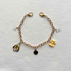 May include: Gold-colored chain bracelet with cartoon dog, paw print, bone, and bow charms. The bracelet has two clasps for easy wear. The charms are in various colors, including yellow, black, white, and green.