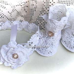Puede incluir: Botas blancas de bebé de ganchillo con una cinta de satén blanca y un botón nacarado. Una diadema blanca de ganchillo a juego con una flor y un botón nacarado.