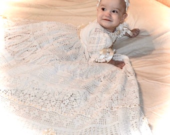 May include: A white crocheted baby dress with a delicate lace pattern. The dress is worn by a baby girl with a white headband.