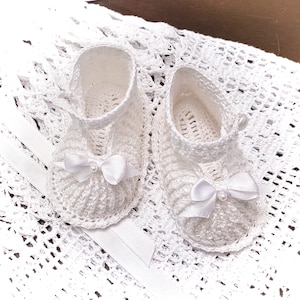 May include: A pair of white crocheted baby shoes with white satin bows and pearl accents.