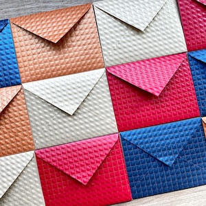 May include: A collection of 12 square envelopes in various colors, including red, blue, gold, and silver. The envelopes have a textured, quilted pattern.