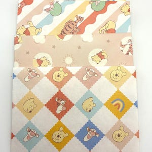May include: A set of four rectangular paper envelopes featuring various Winnie the Pooh character prints. The designs include pastel-colored patterns with Winnie the Pooh, Tigger, and Piglet, incorporating motifs like balloons, rainbows, suns, and stars.