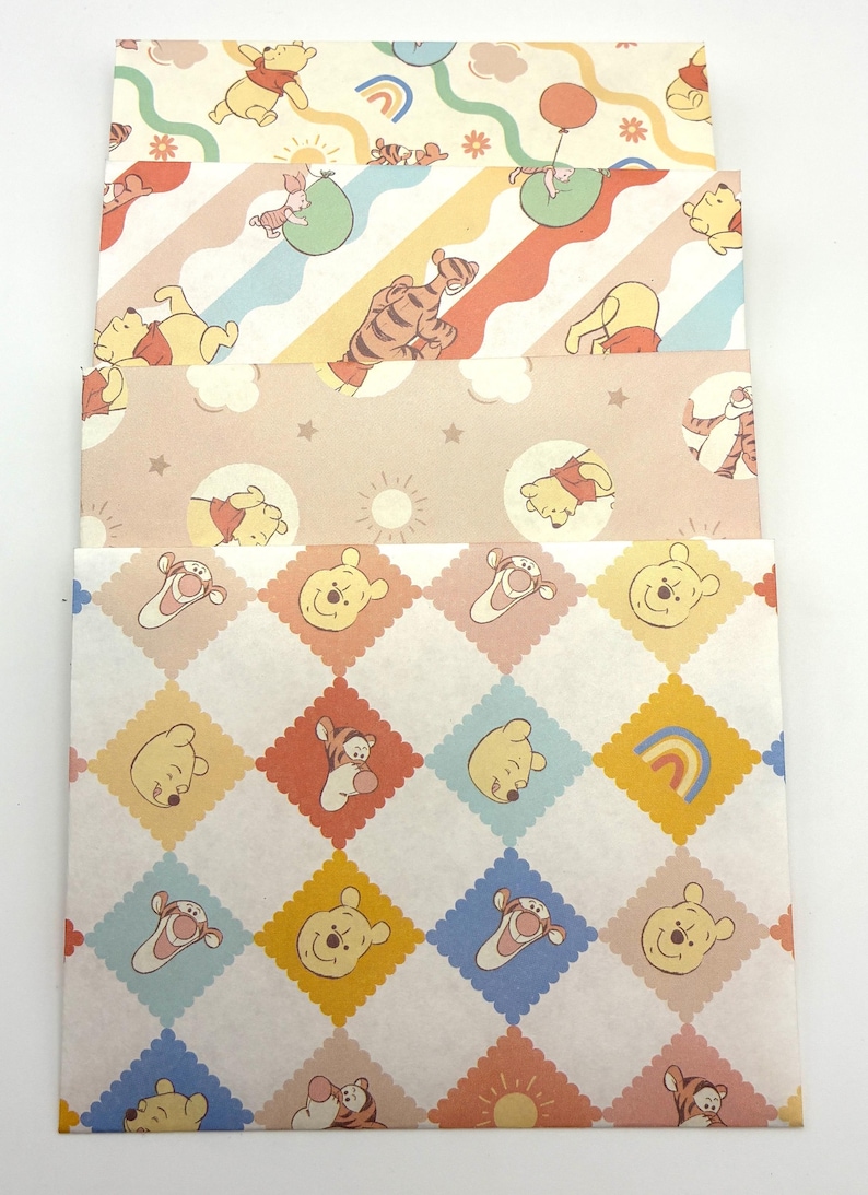 May include: A set of four rectangular paper envelopes featuring various Winnie the Pooh character prints. The designs include pastel-colored patterns with Winnie the Pooh, Tigger, and Piglet, incorporating motifs like balloons, rainbows, suns, and stars.