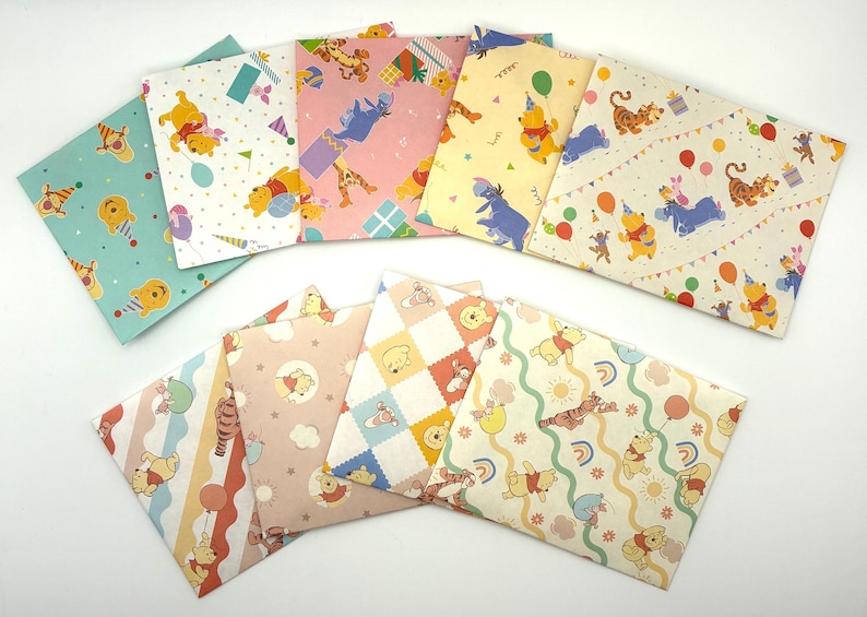 May include: A collection of nine rectangular paper envelopes featuring various Winnie the Pooh character illustrations, including Pooh, Tigger, and Eeyore, with colorful patterns of balloons, party hats, rainbows, and gifts on pastel backgrounds.