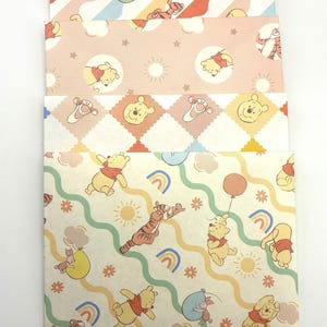 May include: A stack of four rectangular paper envelopes featuring Winnie the Pooh characters. The designs include pastel patterns with Pooh, Tigger, and Piglet, incorporating motifs like rainbows, suns, clouds, stars, and balloons in soft yellow, pink, and blue tones.