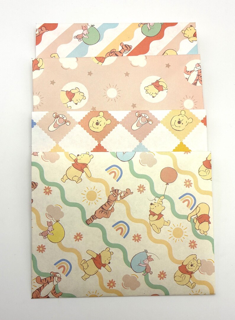 May include: A stack of four rectangular paper envelopes featuring Winnie the Pooh characters. The designs include pastel patterns with Pooh, Tigger, and Piglet, incorporating motifs like rainbows, suns, clouds, stars, and balloons in soft yellow, pink, and blue tones.