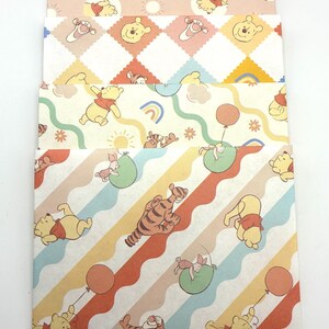 May include: A set of four rectangular envelopes featuring Winnie the Pooh and Tigger characters. The designs include patterns with clouds, stars, suns, rainbows, balloons, and wavy stripes in pastel shades of yellow, orange, blue, and green.
