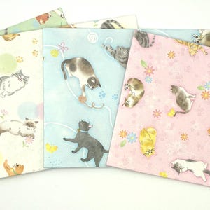 May include: A collection of square paper napkins with cat illustrations. Each napkin features a different pastel color background: green, cream, blue, and pink. The cats are depicted in various poses, with some playing with yarn or toys.