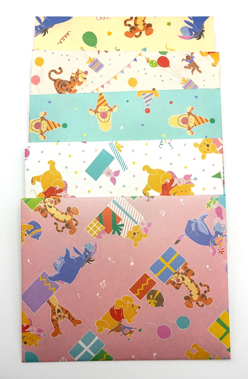 May include: A stack of five rectangular paper envelopes featuring colorful Winnie the Pooh character illustrations. The designs include Tigger, Eeyore, and Piglet with party hats, balloons, and gift boxes on yellow, white, teal, and pink backgrounds.