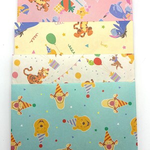 May include: A stack of five rectangular paper envelopes featuring Winnie the Pooh characters. The designs include various patterns with Tigger, Eeyore, and Piglet, decorated with colorful balloons, party hats, gift boxes, and confetti on pastel backgrounds.