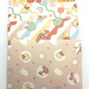 May include: A set of four rectangular paper envelopes featuring Winnie the Pooh characters. The designs include diamond patterns, wavy rainbow lines, and circular motifs with suns, stars, and clouds in pastel shades of yellow, orange, blue, and pink.