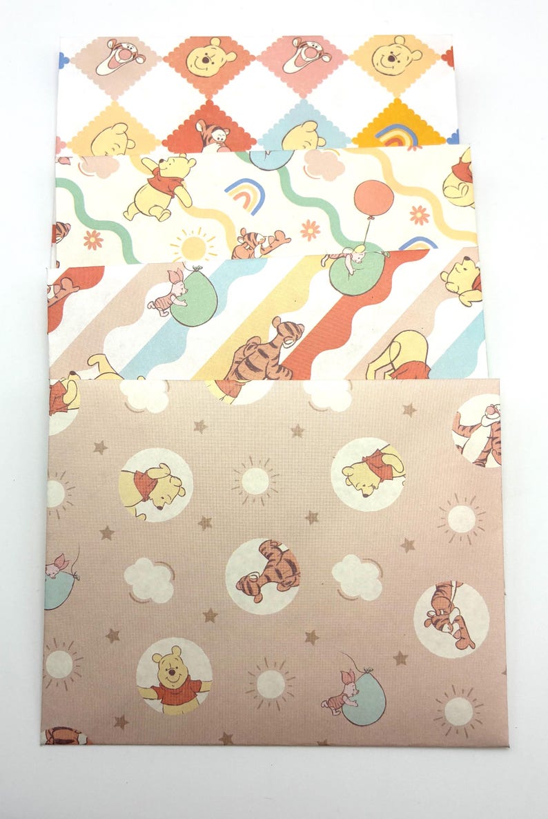 May include: A set of four rectangular paper envelopes featuring Winnie the Pooh characters. The designs include diamond patterns, wavy rainbow lines, and circular motifs with suns, stars, and clouds in pastel shades of yellow, orange, blue, and pink.