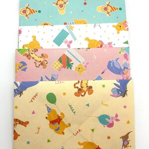 May include: A stack of five rectangular paper envelopes featuring various Winnie the Pooh character patterns. The designs include illustrations of Pooh, Tigger, Eeyore, and Piglet in party themes with balloons, presents, and confetti on cream, blue, white, pink, and tan backgrounds.