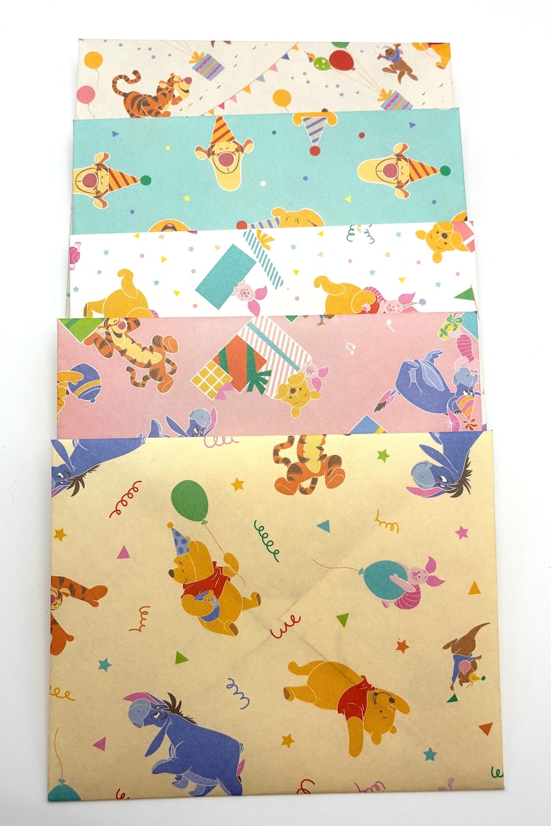May include: A stack of five rectangular paper envelopes featuring various Winnie the Pooh character patterns. The designs include illustrations of Pooh, Tigger, Eeyore, and Piglet in party themes with balloons, presents, and confetti on cream, blue, white, pink, and tan backgrounds.