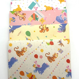 May include: A stack of five rectangular paper envelopes featuring various Winnie the Pooh character patterns. The designs include Tigger, Piglet, Eeyore, and Pooh Bear in party hats with balloons, confetti, and gift boxes in blue, pink, yellow, and tan.