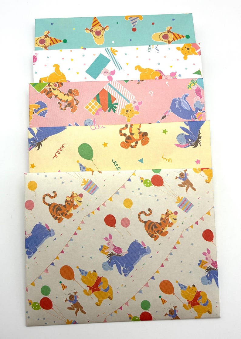 May include: A stack of five rectangular paper envelopes featuring various Winnie the Pooh character patterns. The designs include Tigger, Piglet, Eeyore, and Pooh Bear in party hats with balloons, confetti, and gift boxes in blue, pink, yellow, and tan.