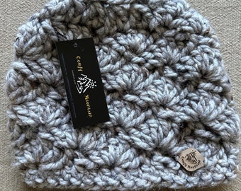 May include: Gray crocheted beanie with a textured pattern. The beanie has a small, round label with the text "Cozy Mountain" on it.