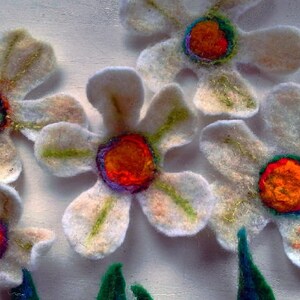 May include: Handmade felt flowers with white petals, gold accents, and vibrant orange, red, and blue centers. The flowers are arranged with green felt leaves, creating a whimsical floral design. Perfect for crafts or home decor.