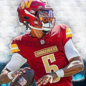 May include: A football player wearing a red and gold jersey with the word "COMMANDERS" on the front and the number "5" on the chest. The player is holding a brown football and wearing a red helmet with a face mask.
