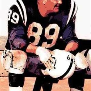 May include: A football player wearing a blue and white jersey with the number "89" on the front. He is sitting on a bench with a football in his hands.