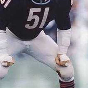 Puede incluir: Un jugador de fútbol americano vistiendo una camiseta azul y blanca con el número 51 en el frente. Lleva un casco y está en posición defensiva.