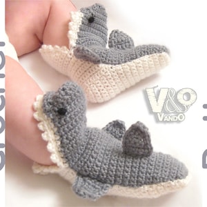 May include: A pair of gray and white crocheted baby booties shaped like sharks. The booties have white crocheted teeth and fins.
