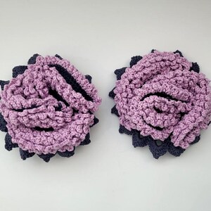 May include: Two crocheted flower embellishments in shades of pink and black. The flowers are made with a textured stitch and have a layered appearance.