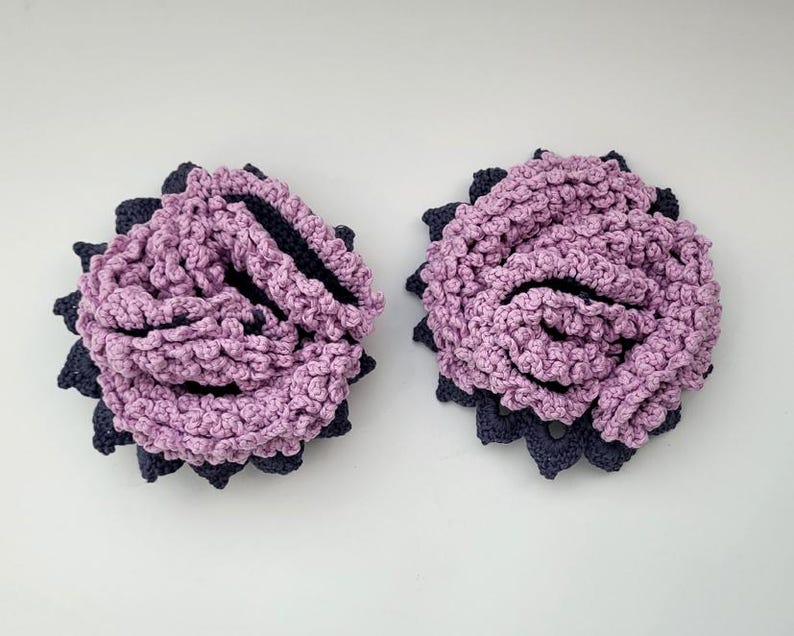 May include: Two crocheted flower embellishments in shades of pink and black. The flowers are made with a textured stitch and have a layered appearance.