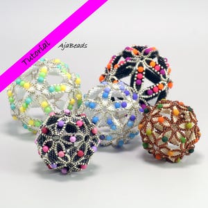 May include: Five beaded sphere ornaments in various colors, including rainbow, blue, black, and orange. The spheres have a geometric openwork design. The image includes the text "Tutorial" and "AjaBeads".