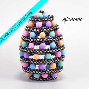 May include: A colourful beaded egg ornament with a layered design. The egg is made with pastel pink, blue, green, and orange beads, and black and gold seed beads. The text "AjaBeads" is visible in the background.