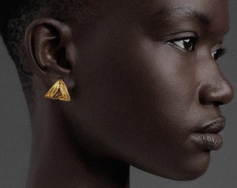 May include: A person with short black hair wearing a white shirt with one shoulder exposed. They are wearing a gold earring in their left ear.