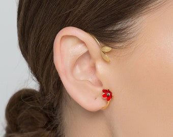 May include: A woman wearing a gold ear cuff with a red flower design. The ear cuff is curved and wraps around the ear.