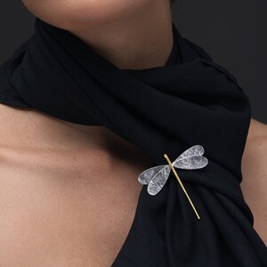Pode incluir: Uma mulher usando um len&ccedil;o preto com um broche de lib&eacute;lula prateado. A lib&eacute;lula tem um corpo dourado e asas transparentes.