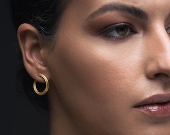 May include: A close-up of a woman's ear with a gold hoop earring. The earring is simple and elegant, with a smooth, polished finish.