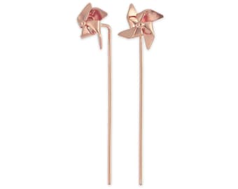 May include: Two rose gold pinwheel-shaped decorative accents. Each pinwheel has four blades and is mounted on a long, slender rod. The pinwheels are a warm, metallic colour and are set against a white background.