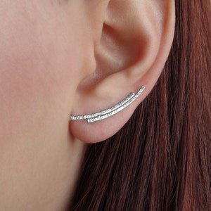 May include: Silver ear cuff with a textured finish. The cuff is curved and has a delicate design.