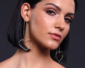 May include: A woman with short black hair wearing a red tank top and gold heart-shaped earrings.